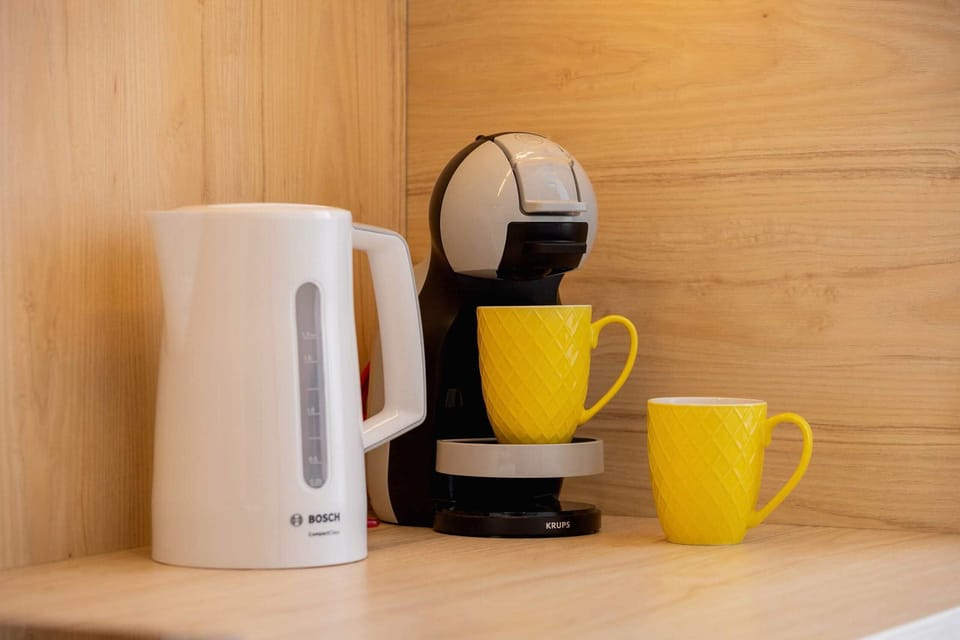 A close-up of a coffee corner featuring a coffee machine, a kettle, and two yellow mugs.
