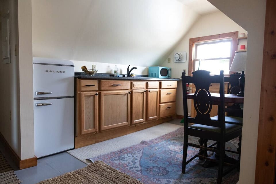 Cozy dining area with antique table and chairs, dishware, sink, and mini fridge. Kitchen includes Instant Pot, air fryer, toaster, hot plate, microwave, and cookware.