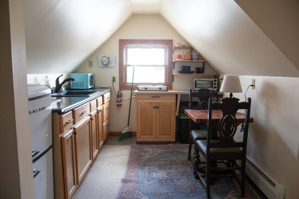 Cozy dining area with antique table and chairs, dishware, sink, and mini fridge. Kitchen includes Instant Pot, air fryer, toaster, hot plate, microwave, and cookware.