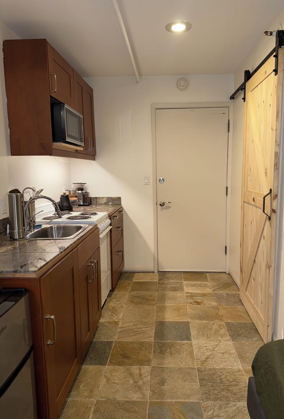Kitchen with microwave, mini fridge, electric stove/oven with cooking utensils.