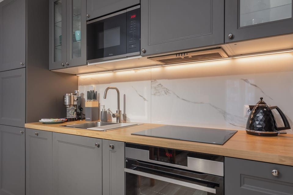 A modern kitchen with gray cabinets, built-in appliances, and a well-lit countertop.
