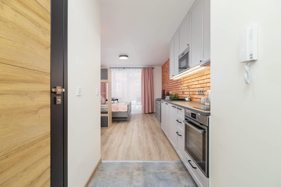 A bright hallway with a modern kitchenette featuring a brick backsplash and sleek appliances.
