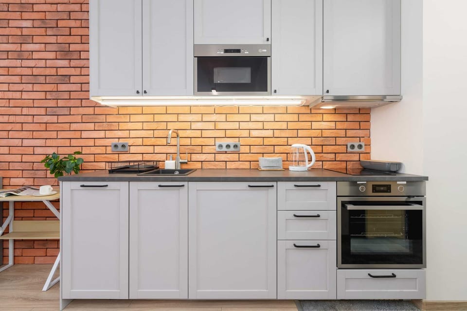 A modern kitchenette with gray cabinets, a brick backsplash, and a built-in oven.
