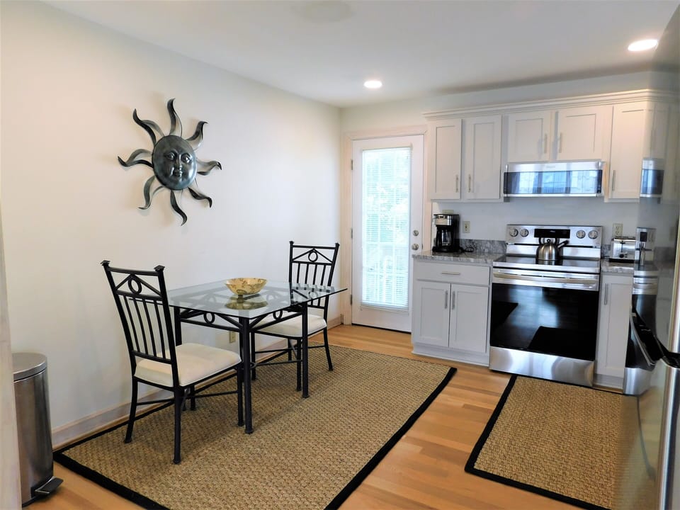 9 South Seventh Street - Modern Kitchen and Dining Area - A view of the kitchen featuring stainless steel appliances (oven and microwave), white cabinetry, and a small dining table with chairs on a natural fiber rug.