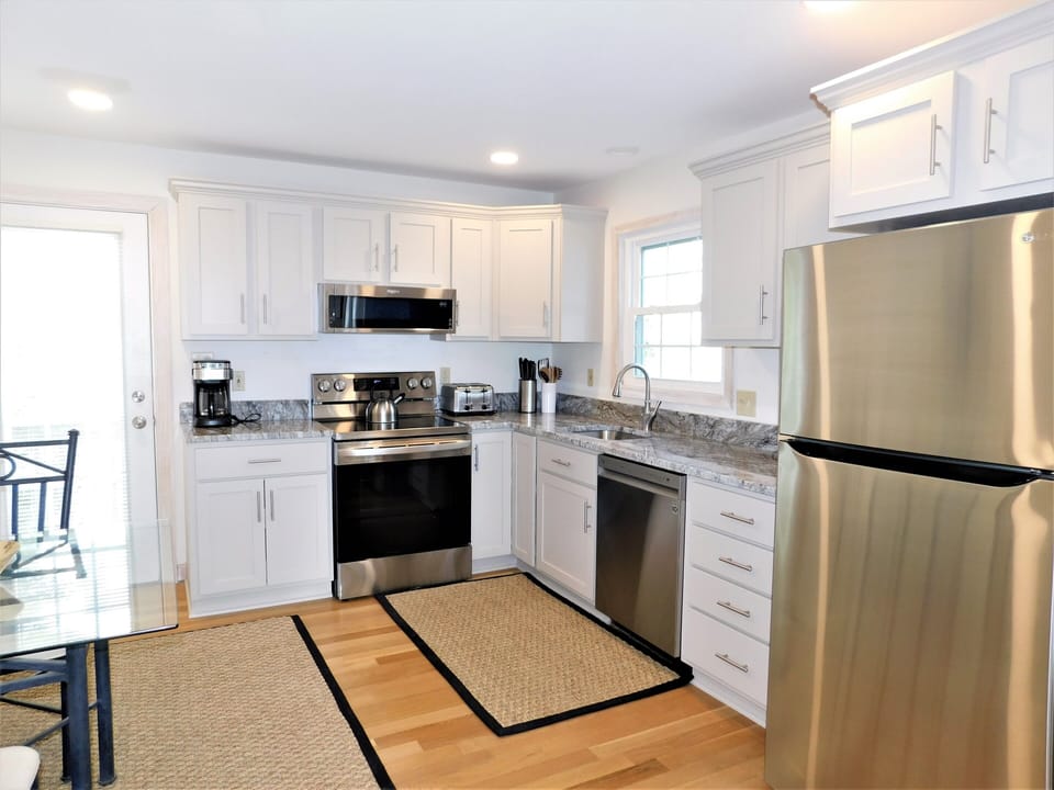 9 South Seventh Street - Full Kitchen View - A wider angle of the kitchen showing the stainless steel refrigerator, white cabinets, and dishwasher, set against light hardwood floors.