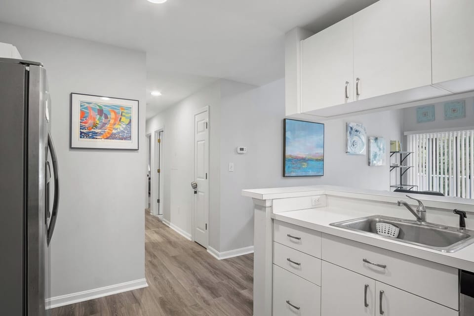 54021 Sand Dollar Court - Kitchen - Alternative view of the kitchen highlighting the clean white countertops, integrated sink area, and a hallway lead-in accented by coastal wall art.