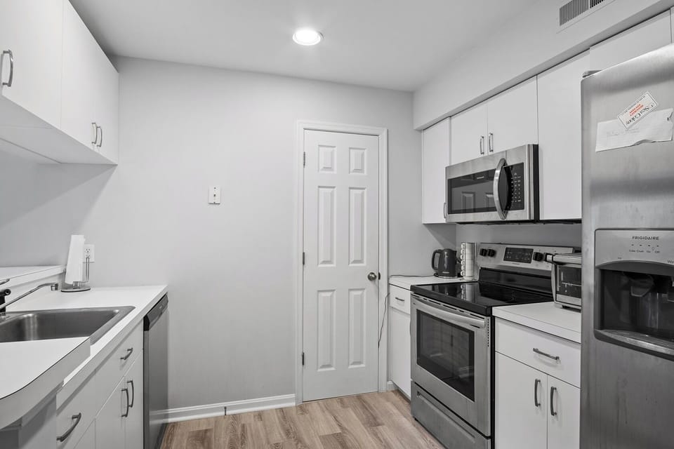 54021 Sand Dollar Court -Kitchen - Modernized kitchen featuring sleek white cabinetry, stainless steel appliances including a built-in microwave and glass-top range, and light wood-plank flooring.