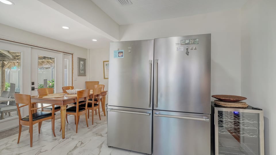 Open dining area with wood table and chairs adjacent to the kitchen with stainless steel refrigerator