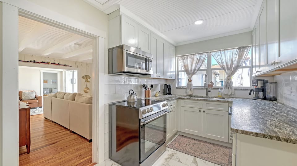 Wide-angle view of the kitchen with white and gray cabinetry, open to the main living area