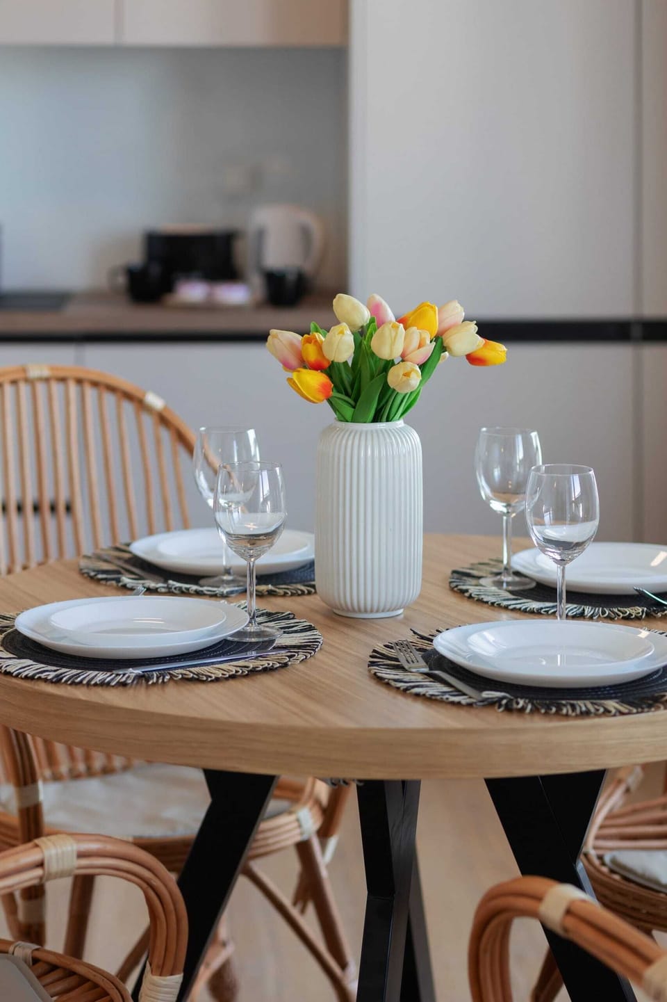A close-up of a dining table set with elegant plates, cutlery, and fresh flowers in a vase.
