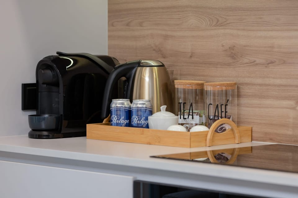 A close-up of a coffee station with a kettle, coffee maker, and mugs, arranged on a wooden tray.
