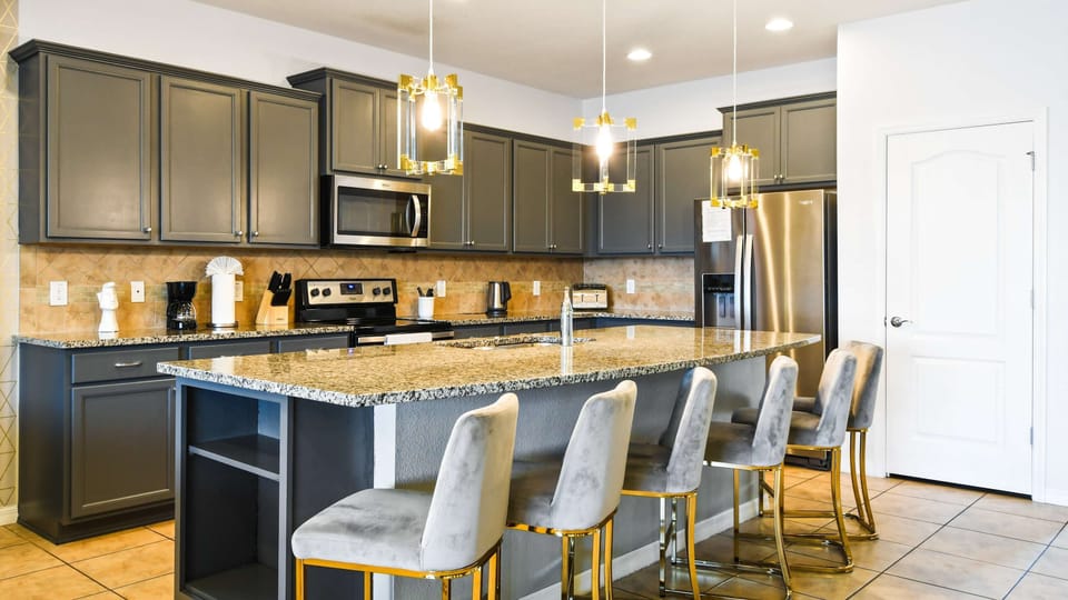 Modern kitchen with granite counters, stainless steel appliances, and gold lighting.