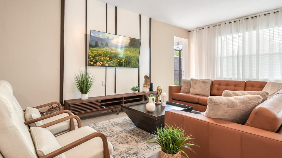 Stylish living room with warm leather seating, airy curtains, and a nature-inspired TV.