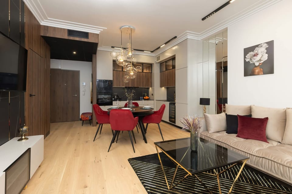 A spacious dining and living area with a chandelier, red chairs, and warm wooden floors.

