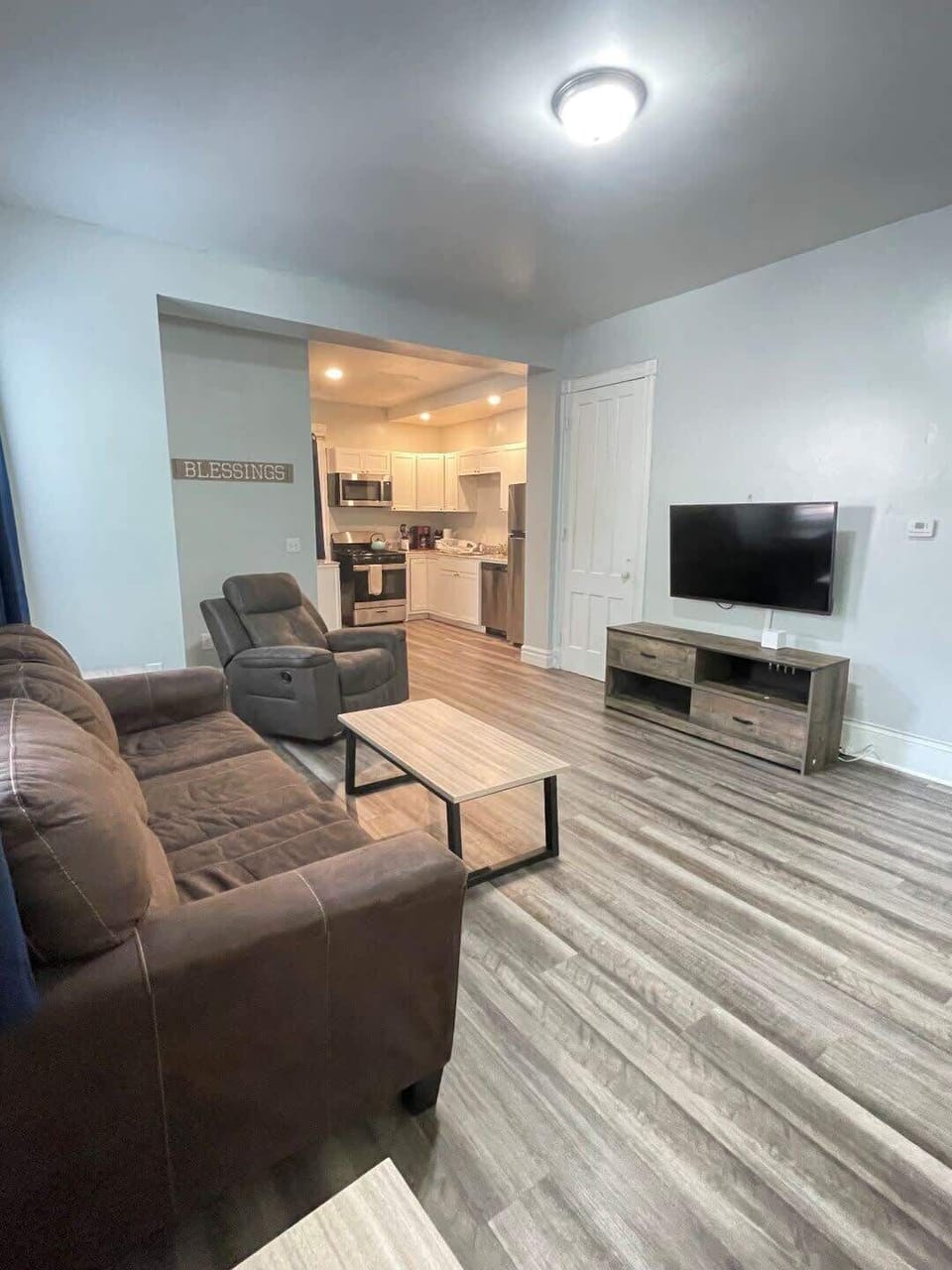 Spacious living area flowing into a sleek kitchen, featuring large windows, a comfortable couch, and a recliner.