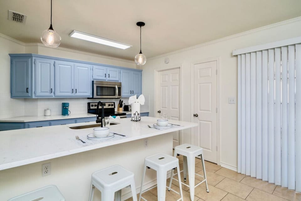 This kitchen is ready for both quick bites and full meals. Gather at the island for coffee or casual dining, while stainless steel appliances and soft blue cabinets create a cheerful vibe. Stocked with cooking utensils, starter spices, and all the essenti
