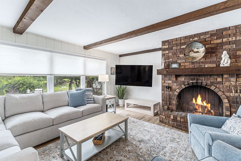 The den is complete with a large sofa, armchairs, a smart TV, and a beautiful woodburning fireplace