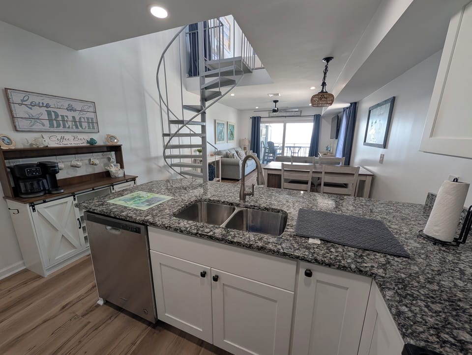 Picture yourself whipping up meals on sleek counters, then gathering around the dining table as sunlight streams through windows framing your coastal escape. The spiral staircase adds charm to this bright, open retreat.