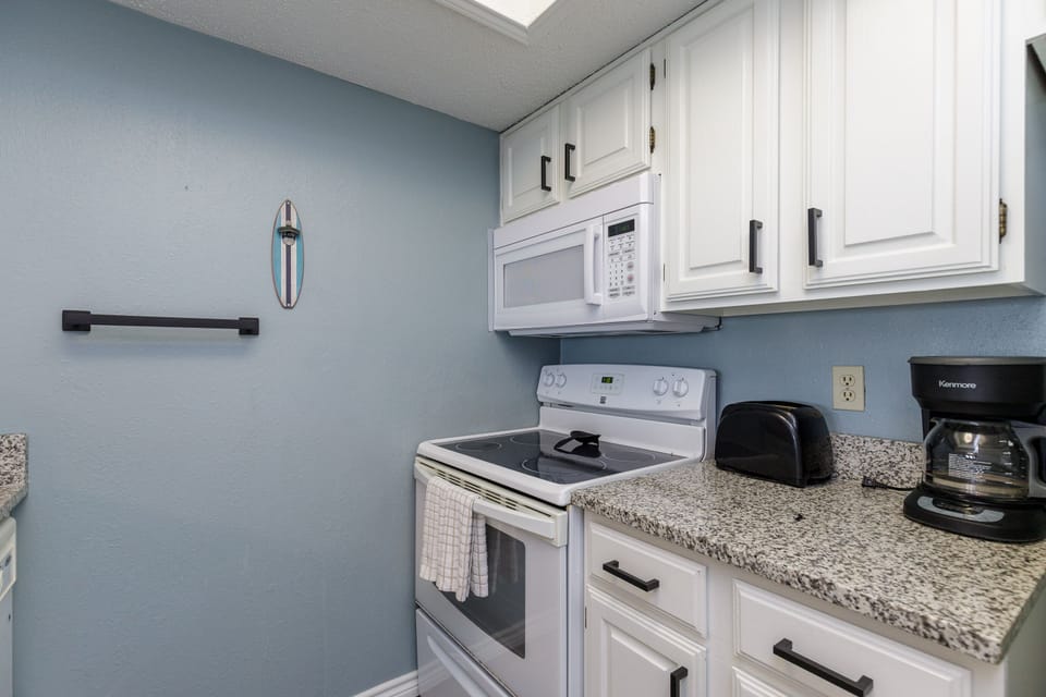 Your fully equipped kitchen features granite countertops, white appliances, and soothing blue walls. Everything you need for home-cooked meals during your stay.
