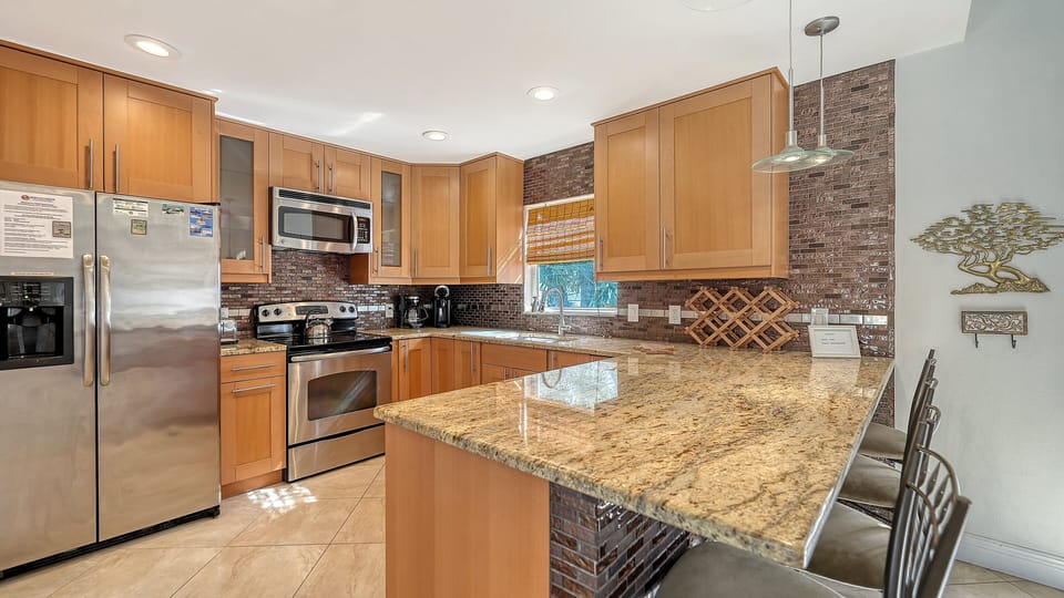 Gourmet kitchen with large granite island, stainless steel appliances, and stone tile backsplash