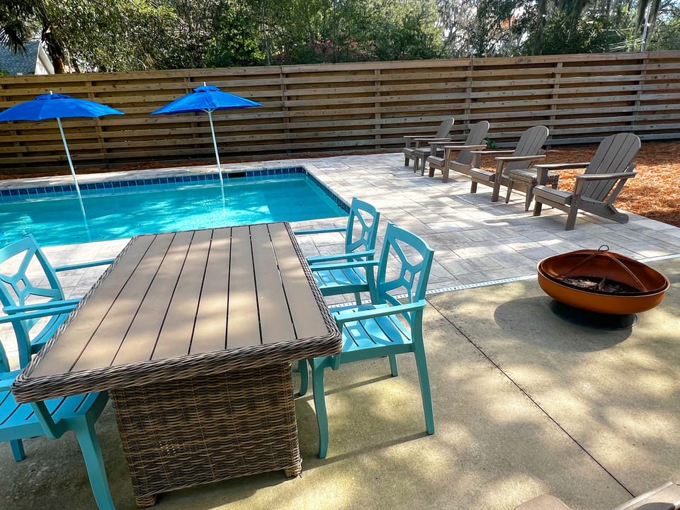 Poolside Dining And Firepit - Backyard dining table, firepit bowl, lounge chairs, umbrellas, and fenced pool area for outdoor meals and evenings.