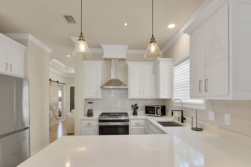 Kitchen With Stainless Appliances - Second kitchen angle with gas range, hood vent, quartz counters, tile backsplash, and full-size refrigerator.