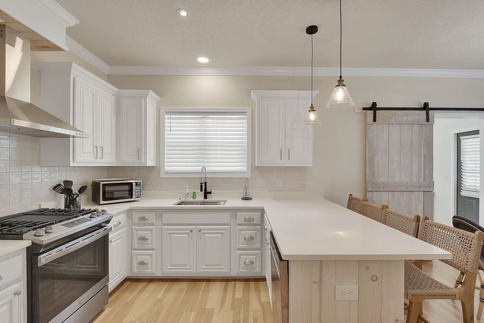 Kitchen Island With Gas Range - Kitchen with quartz counters, gas range, stainless appliances, white cabinetry, and island seating for casual meals.