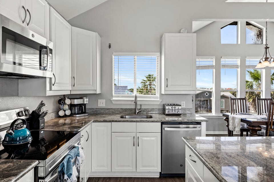 Bright chef's kitchen with modern appliances, large windows, granite countertops, and direct access to the outdoor deck and dining area.