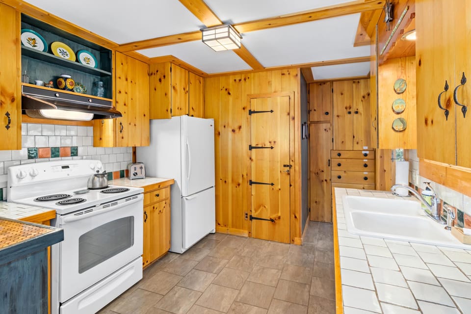 Galley kitchen with knotty pine cabinetry, white tile countertops, electric stove, and white refrigerator.