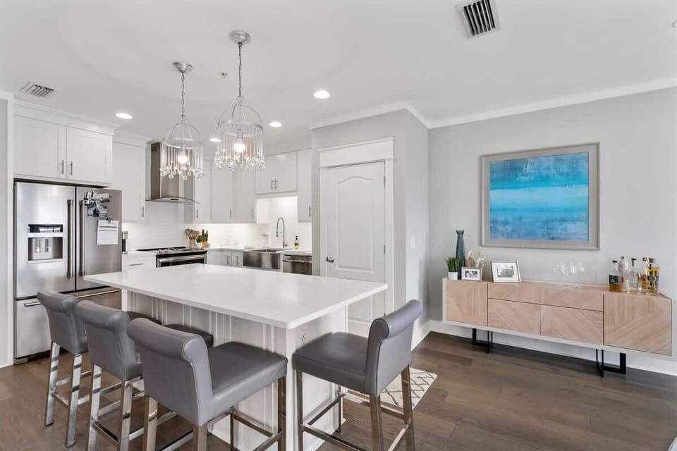 - Sleek kitchen features quartz countertops, pendant lighting, and stainless steel appliances - Oversized island with seating for four is perfect for casual dining or morning coffee - Modern sideboard and beachy art add a coastal touch