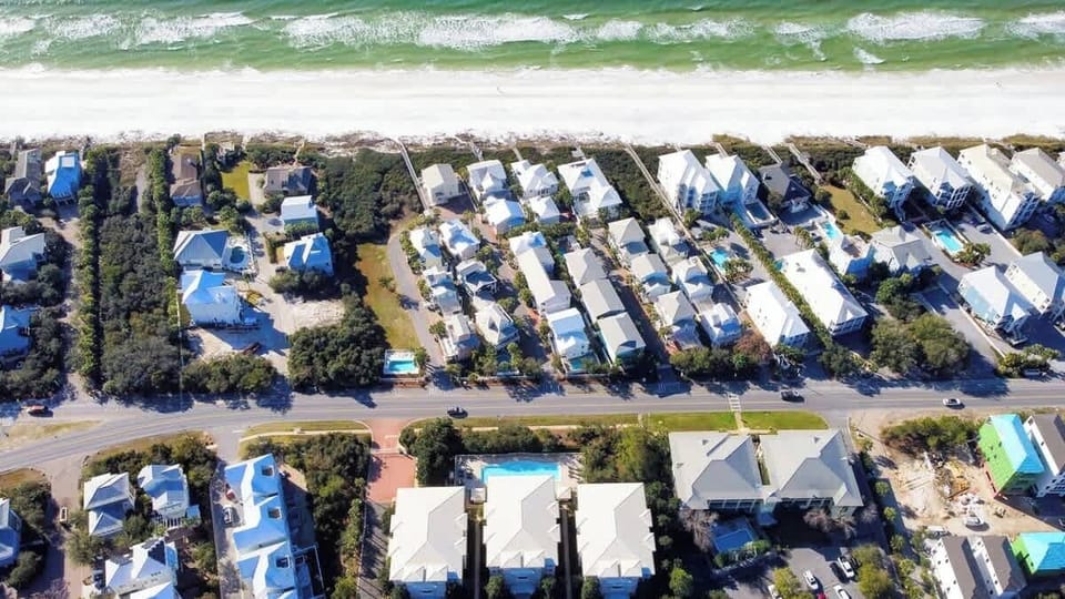 Beautifully arranged coastal homes line the shore, just steps from the soft white sand and emerald waves.