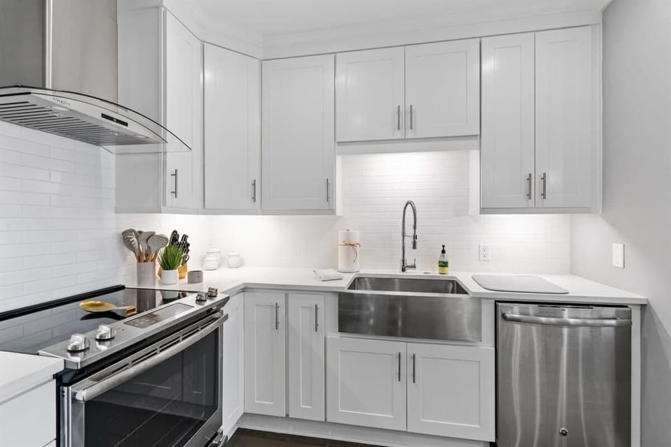- Sleek white cabinetry surrounds a deep stainless steel sink with modern fixtures - Glossy subway tile backsplash reflects under cabinet lighting for a polished touch - Streamlined appliances and open counter space invite easy meal prep