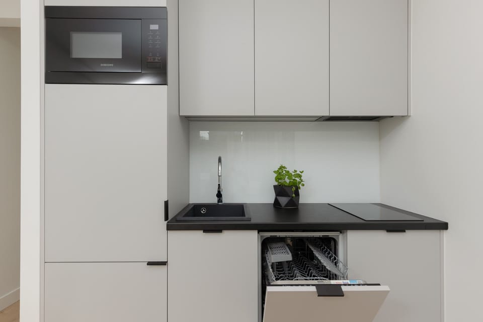 A clean, modern kitchenette with a black countertop and built-in appliances.
