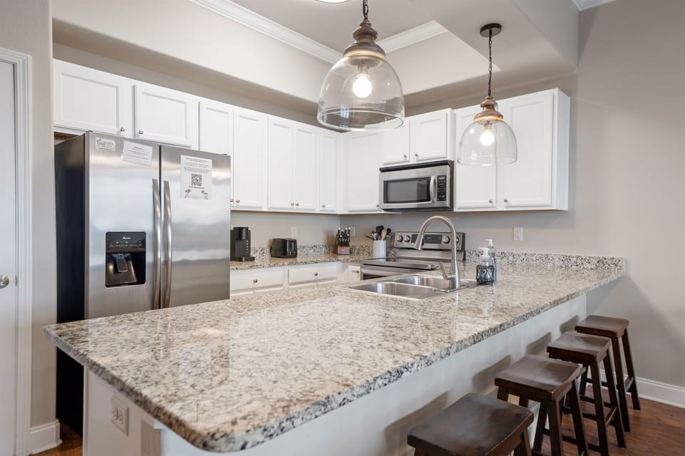 Fully equipped kitchen with granite counters, stainless appliances, and bar seating for casual breakfasts or cocktails.