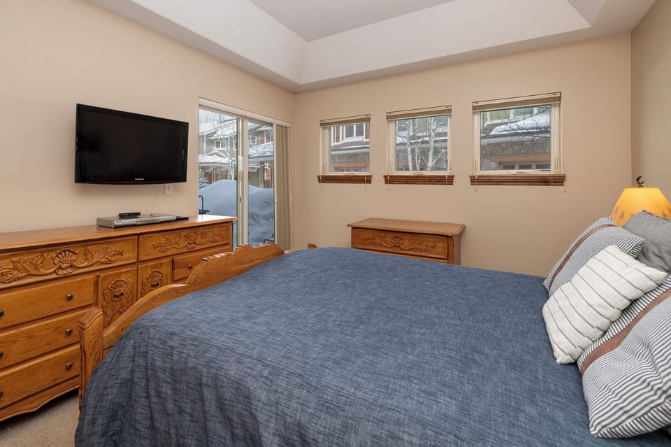 Unwind in your cozy bedroom featuring snowy mountain views and warm wood furnishings for the perfect alpine retreat.