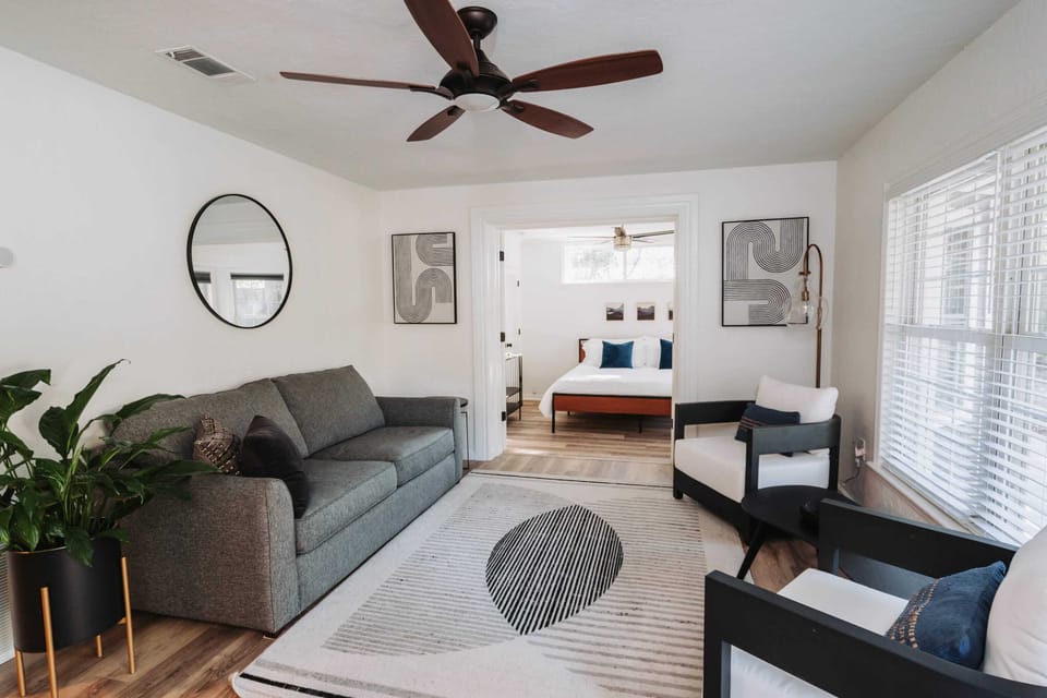 Relax in a bright, thoughtfully curated living area featuring designer touches, lush greenery, and a seamless transition into the primary suite. Perfect for those who appreciate clean lines and a peaceful atmosphere.