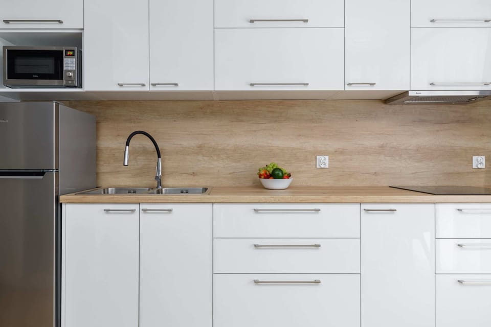 A closer look at the contemporary kitchenette, highlighting the sink, microwave, and seamless white cabinetry.