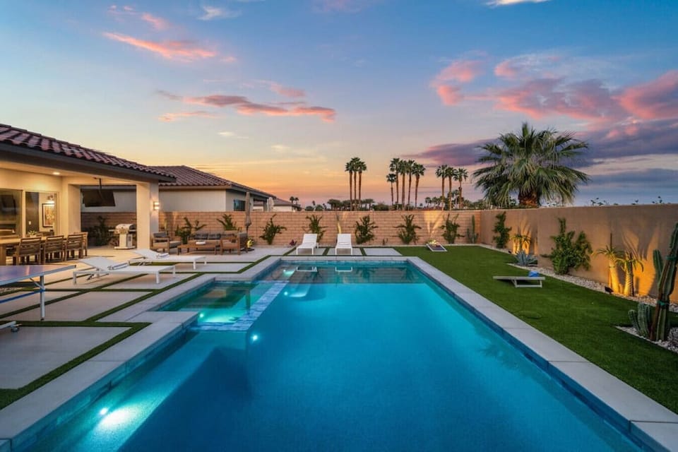 Sparkling pool at sunset w/ lounge seating, palm trees & glowing skies overhead