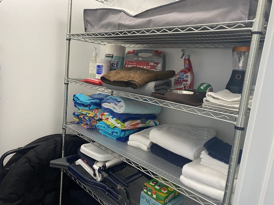 Hallway closet with beach towels, extra bath towels, pet blanket for furniture, high chair, portable play crib, First Aid kit, vacuum, mop