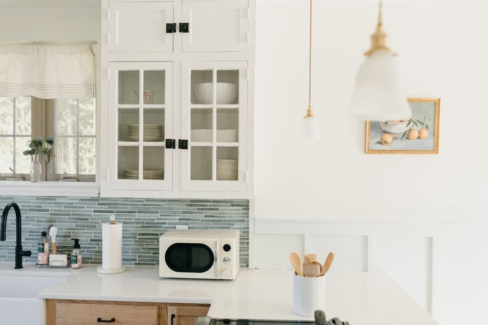 Kitchen counter with white cabinets, microwave, utensils, and fruit artwork