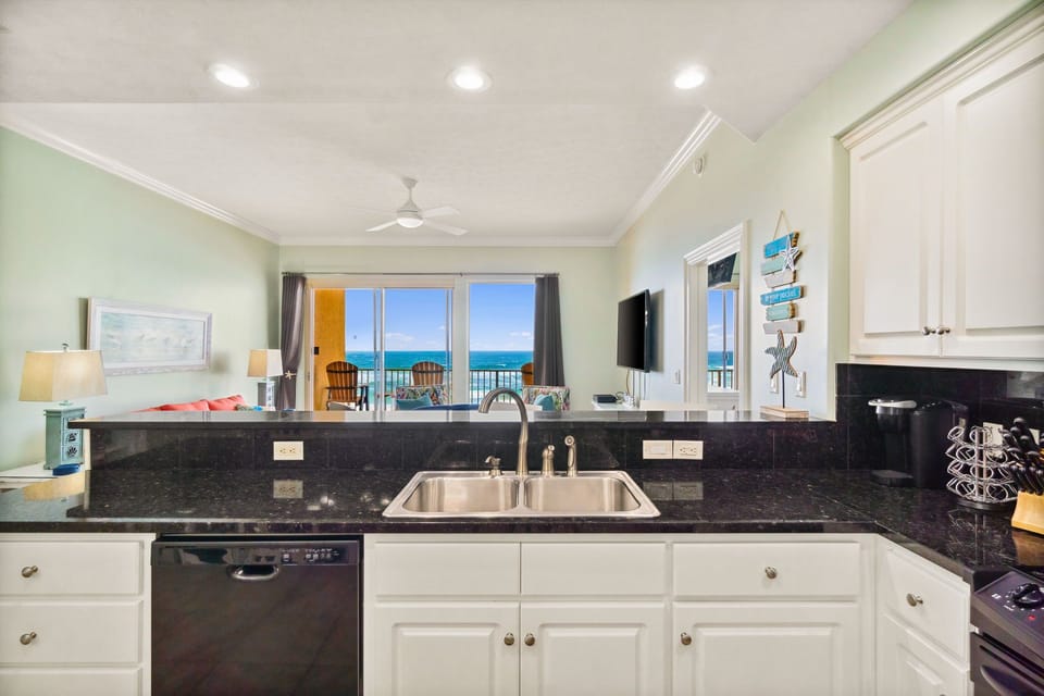 Kitchen sink area w/ dark countertops, ocean views & plenty of prep space for cooking together.