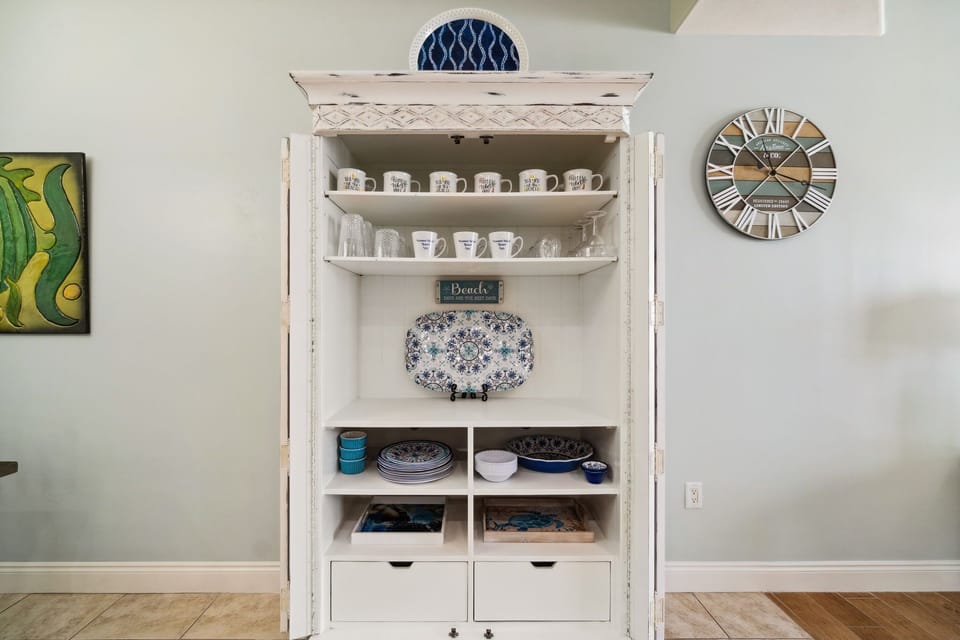 Thoughtfully styled kitchen nook w/ open shelving, folded linens & decorative coastal touches.