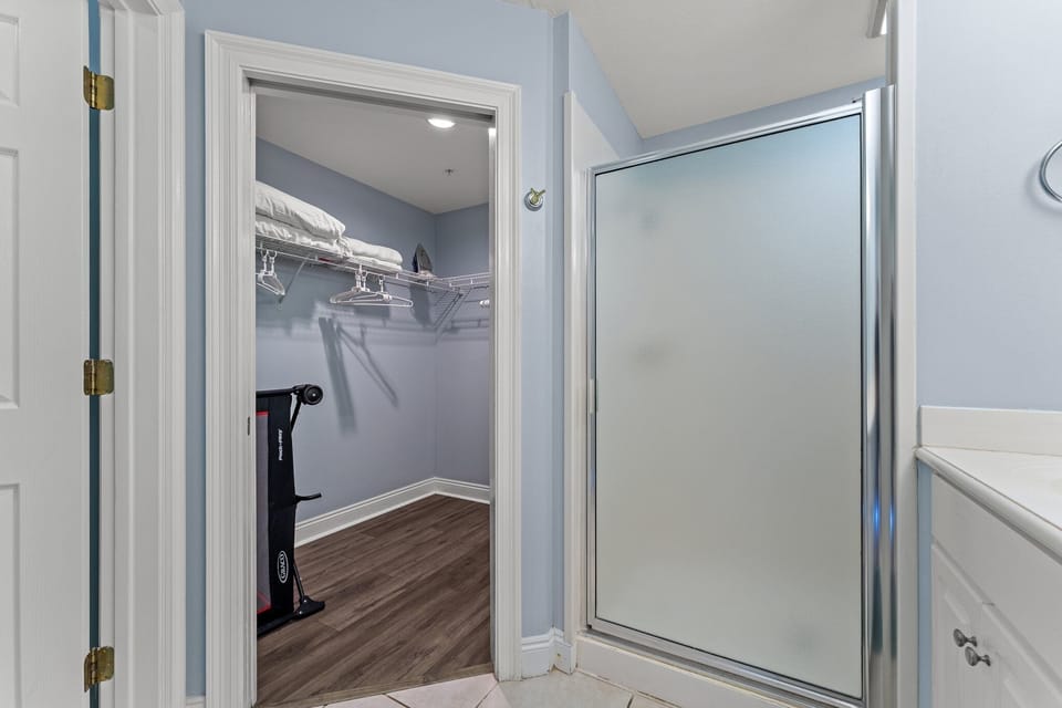 Walk-in closet adjacent to a modern bathroom with a glass shower enclosure.