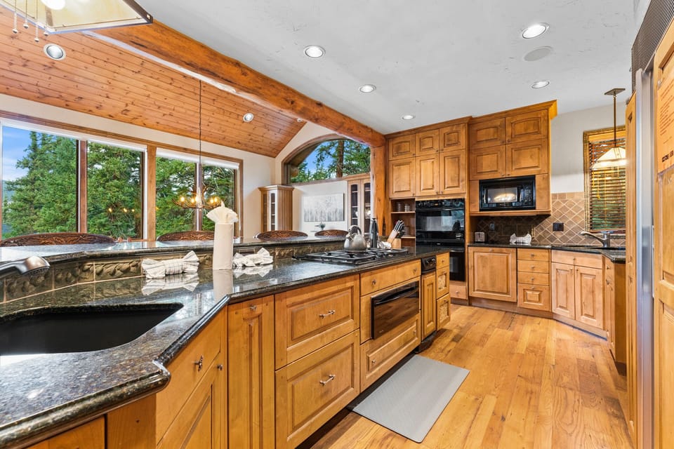 Your gourmet kitchen features rich wood cabinetry, granite counters, and forest views through expansive windows - perfect for cooking memorable meals.
