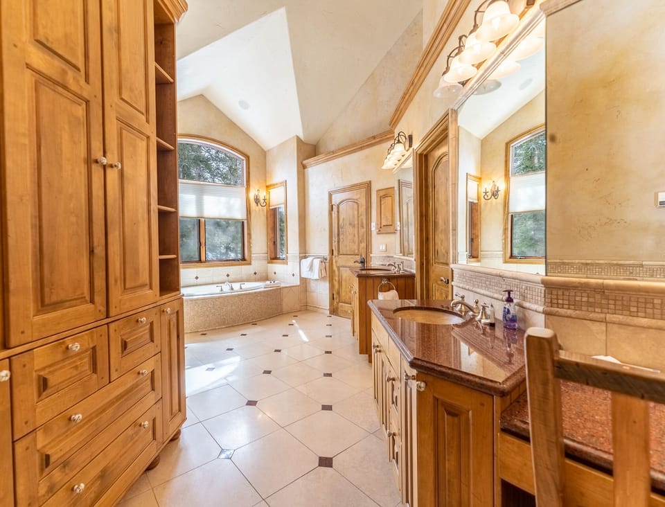 Step into your luxurious master bathroom featuring rich wood cabinetry, dual vanities, and a relaxing soaking tub surrounded by elegant stonework.