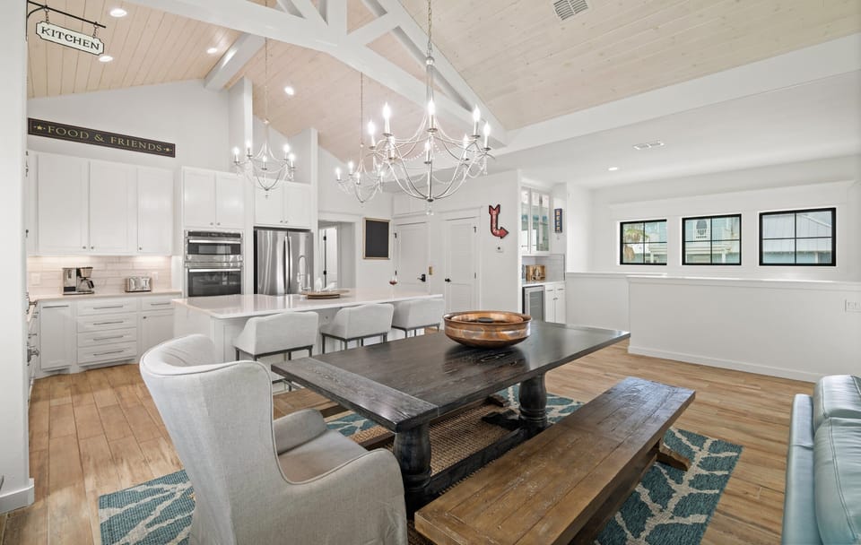 Dining & Kitchen — Farmhouse Table, Gray Wingback Chairs, Chandeliers, 'Kitchen' Sign & White Cabinets