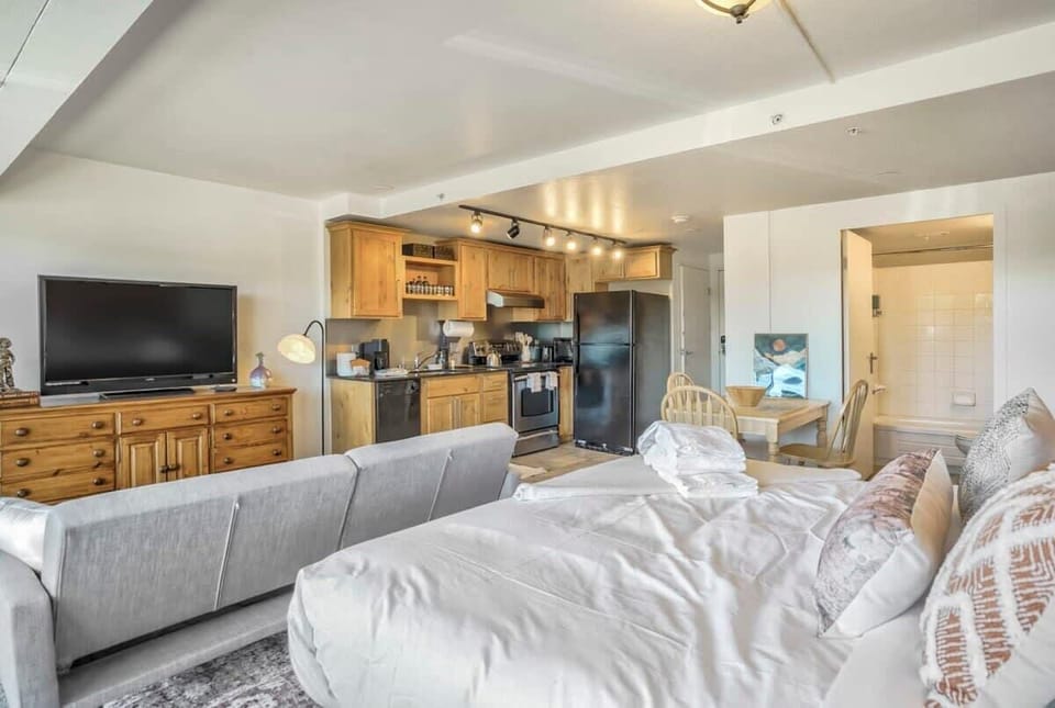 A relaxed living area with comfortable seating, a TV, and warm wood accents, flowing naturally toward the kitchen. It’s set up for slow mornings on the couch or winding down together after a full day out.