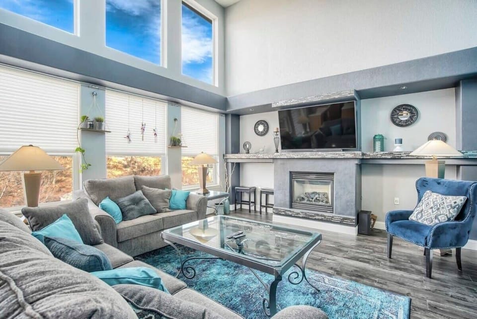 Sunlight pours through tall windows into this airy living room where soft gray seating surrounds a glass coffee table and fireplace. Settle in with a drink, stretch out on the sofa, and enjoy relaxed conversations in this bright, open gathering space