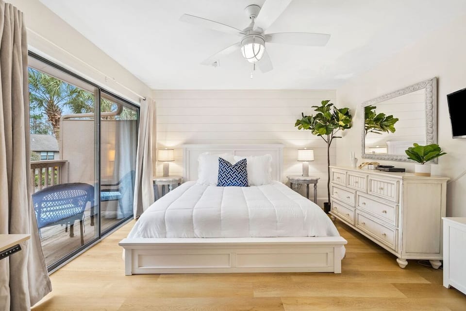 A spacious and grand master bedroom equipped with a flat screen TV, private balcony, and standing/sitting desk and workspace. 