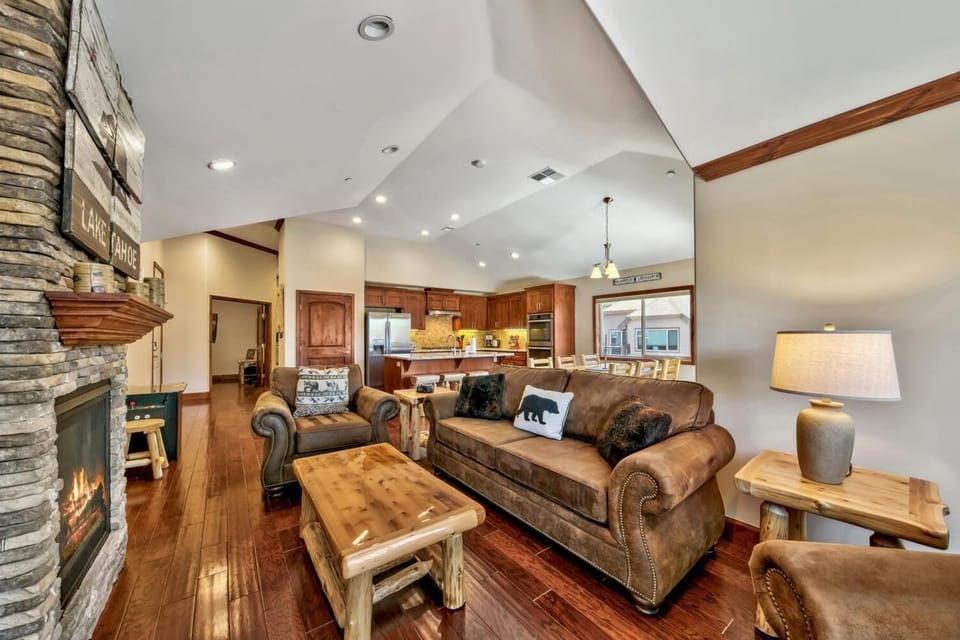 Cozy up in your mountain retreat living room with leather seating by the stone fireplace, open kitchen nearby.